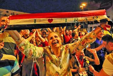 Varios ciudadanos iraquíes celebraron en las calles. Una mujer sostiene la bandera de su país con el lema "yo amo Irak".