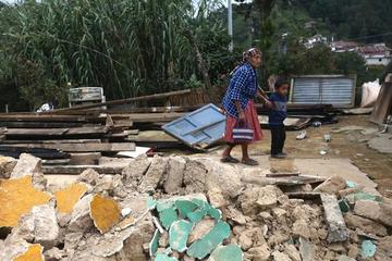 Una anciana camina junto a su nieto por los escombros de su casa.