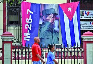 Dos personas caminan junto a un lienzo con la imagen del fallecido líder cubano Fidel Castro en una calle de La Habana.