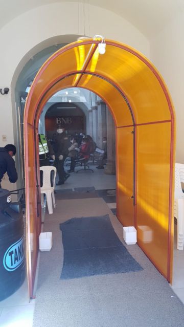 Está en la entrada a la entidad bancaria.