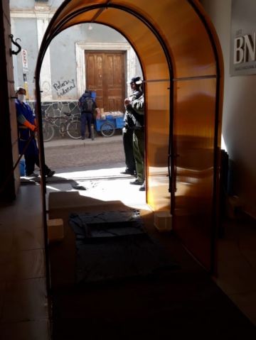 Está en la entrada a la entidad bancaria.